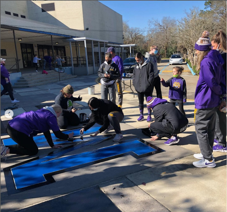 LSU softball team members cleaning the outside of a high school building