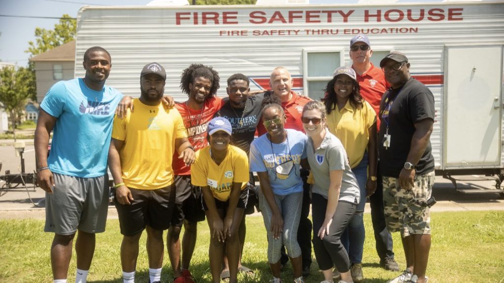 LSU and Southern student-athletes pose with volunteers in front of a fire safety trailer.