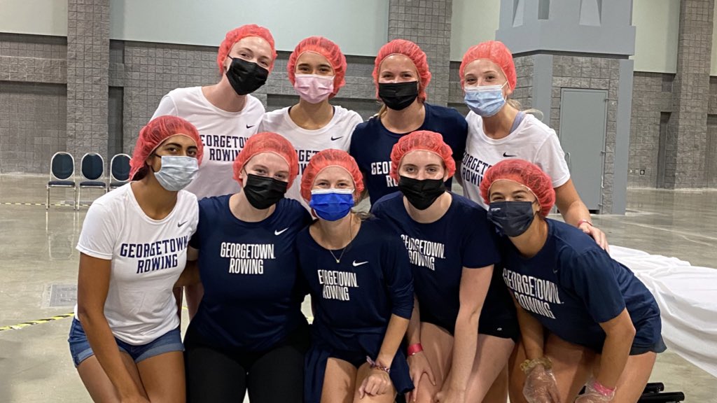 Nine members of the Georgetown rowing team pose with face masks on and hairnets at a food distribution center.