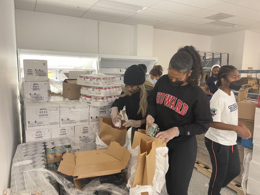 Howard University student-athletes wear masks at an indoor food pantry facility and pack grocery bags.