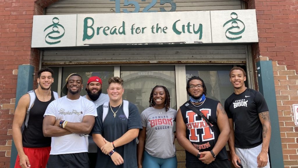 Howard University student-athletes pose outside of the Bread for the City building, all smiling.