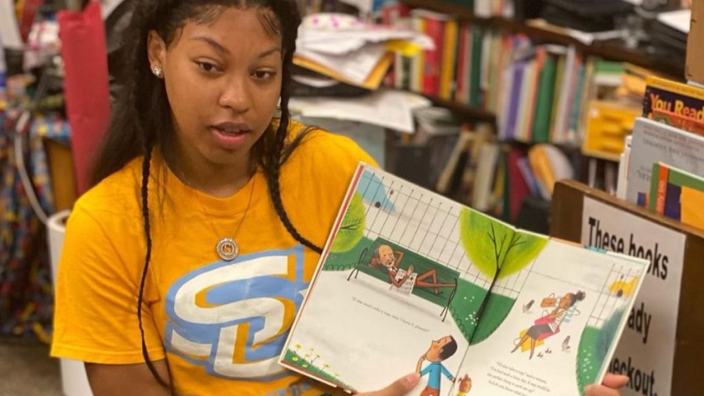 A Southern University student-athlete holds a childnren's book to show the inside to elementary school students (not in the frame).