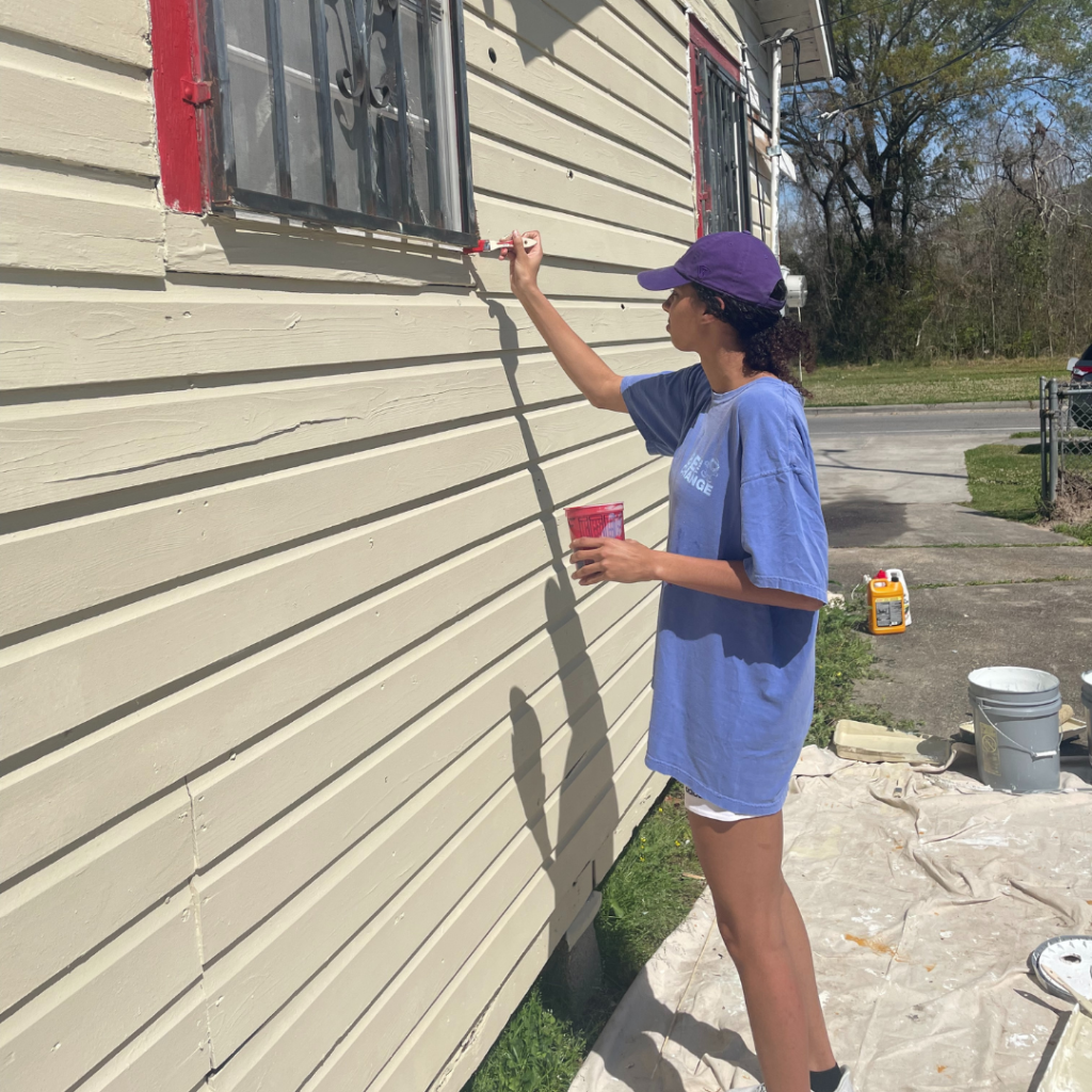 An LSU student-athlete paints the side of a house.
