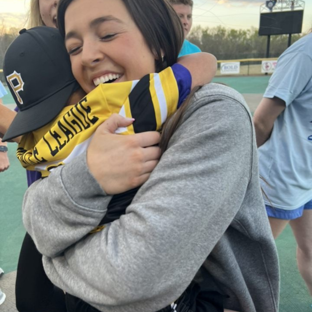 An LSU athlete is smiling with her eyes closed, hugging a young Miracle League athlete. 
