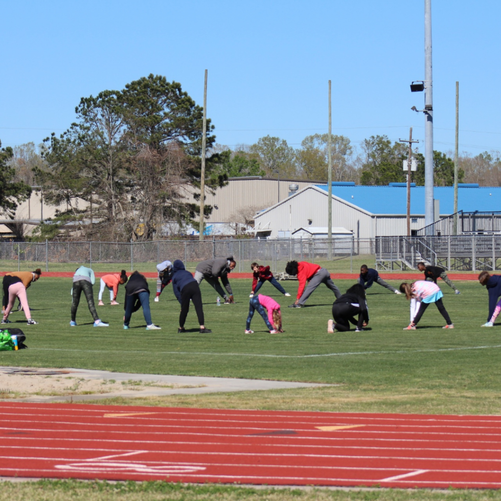 A group of people stretching in a circle on a field with a track around them.
