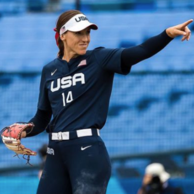 Monica Abbott in her Team USA Softball uniform, smiling, and looking and pointing to her left.