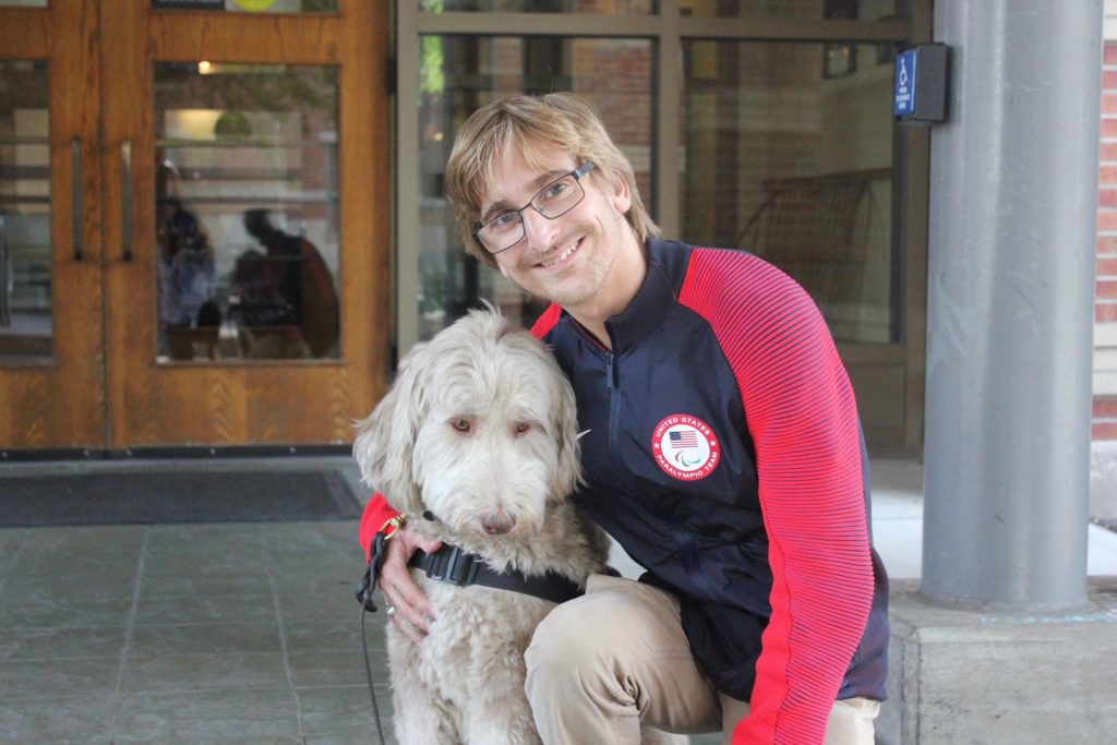 Ayden is smiling at the camera with his arm around a dog.