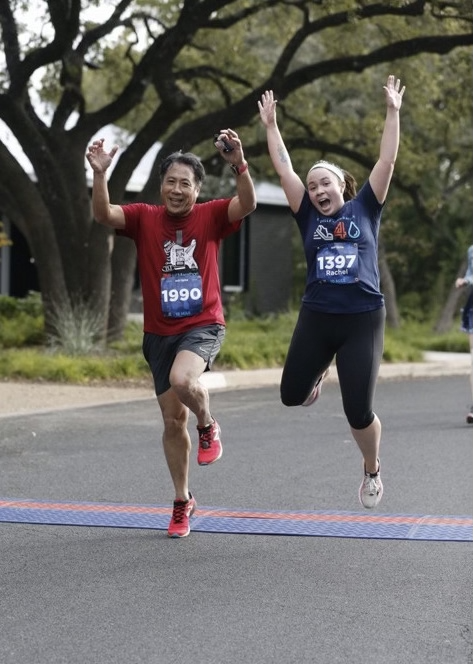 Rachel and her dad running across the finish line of a running race. 