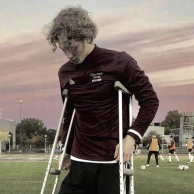 Mattis standing with crutches on a soccer field, looking down