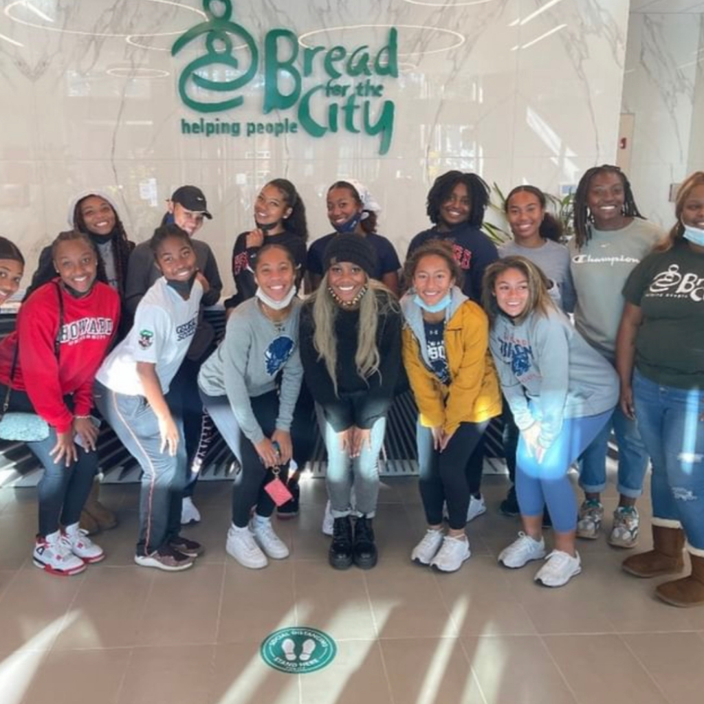 Members of the Howard Women's soccer team pose in front of the Bread for the City sign at their facility