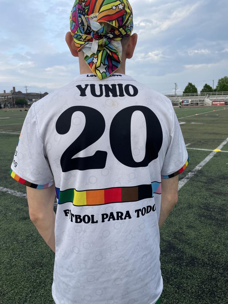 a soccer player stands with their back to the camera showing off their jersey that says "yunio" and "futbol para todos"