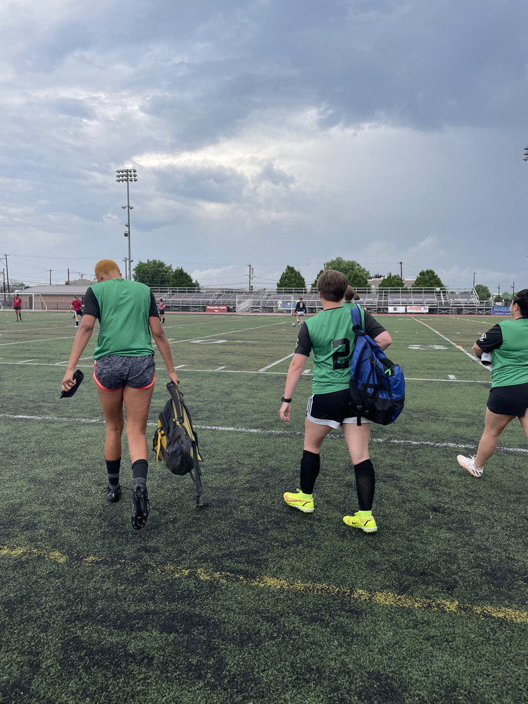 three soccer players with their backs to the camera walk across the field after a game