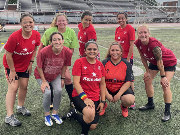 8 soccer players pose on a soccer field in their uniforms