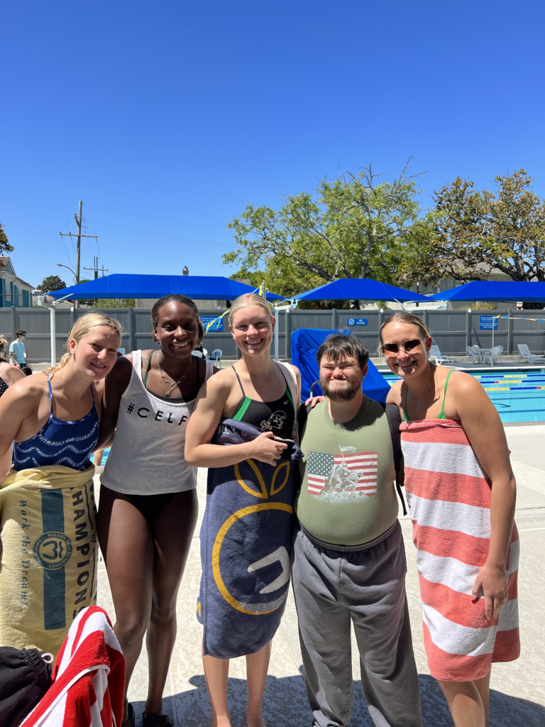 4 Tulane Student Athletes and one special olympics athlete pose next to a pool while standing and smiling at the camera. 