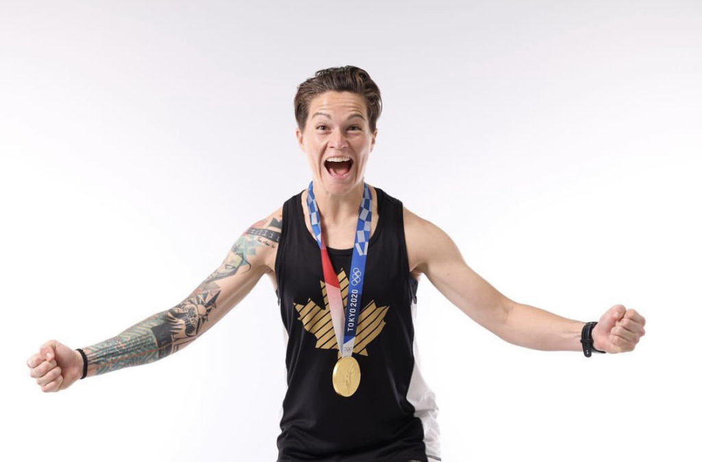 Erin McLeod faces the camera cheering with her arms open and Olympic gold medal around her neck.