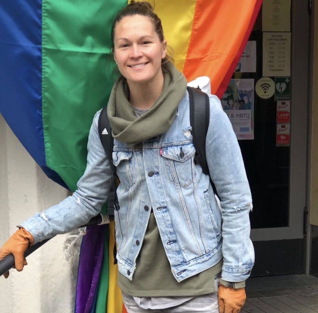 Erin McLeod standing in front of a gay pride flag and smiling