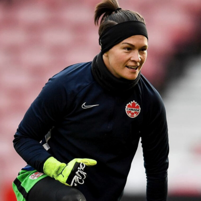 Erin McLeod wearing her Team Canada warm up gear, kneeling on a soccer field