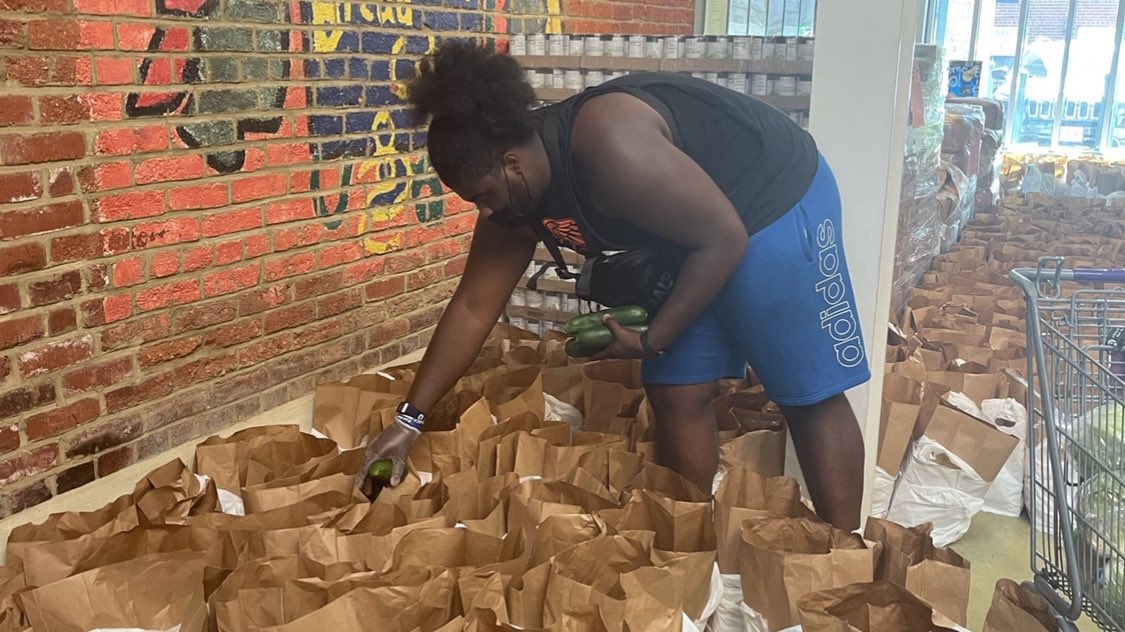 A Howard University football player leans over many open paper grocery bags and it putting items in one.
