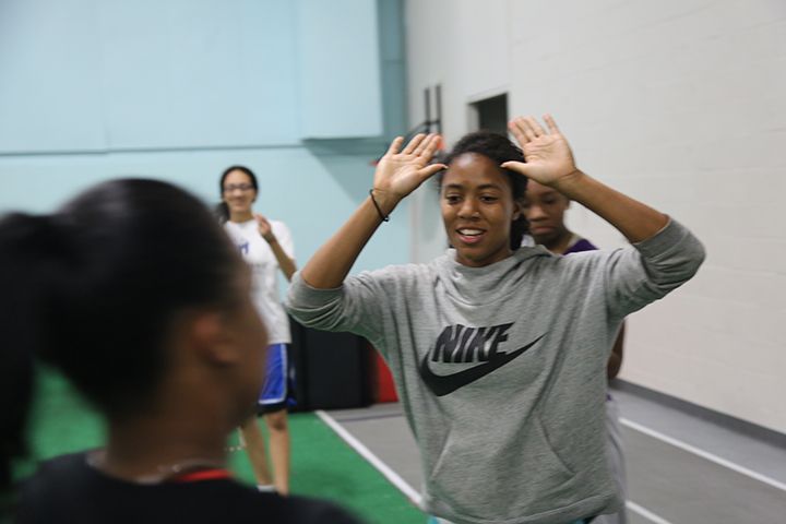 Kori is holding both of her hands up and smiling, trying to high five another person off camera. 