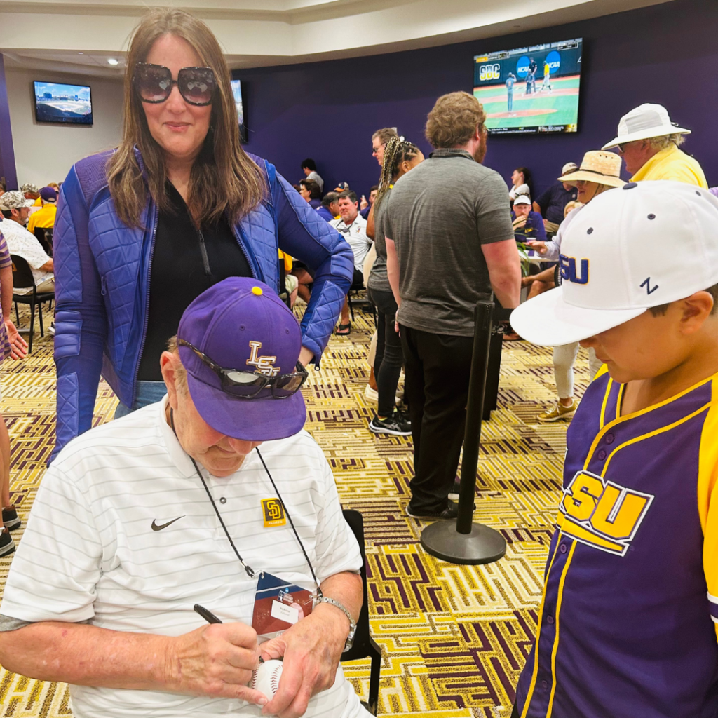 Skip Bertman signs a baseball for a young fan while Lori Bertman watches and smiles
