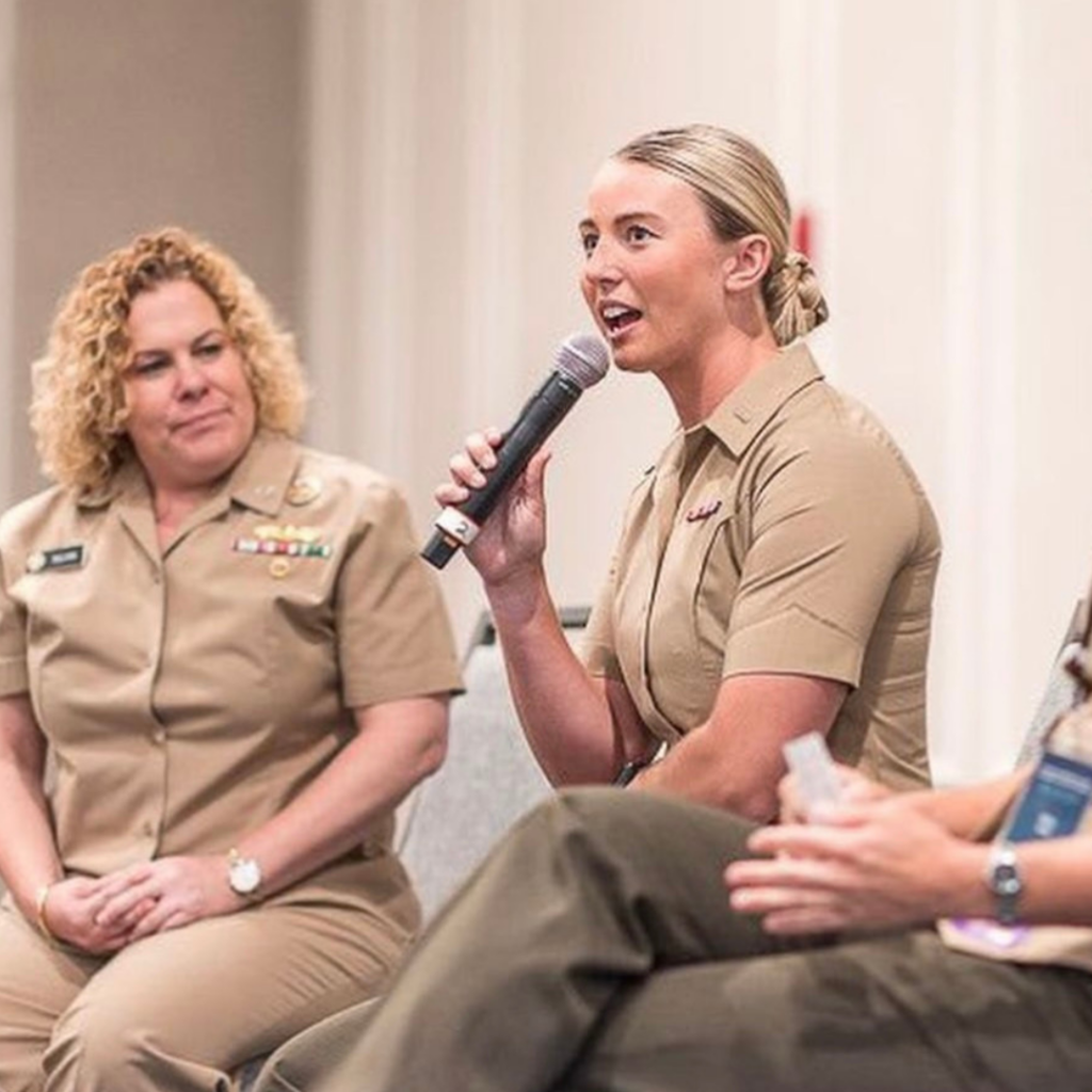 Photo of Riley Tejeck talking into a microphone in her military uniform during a panel session.