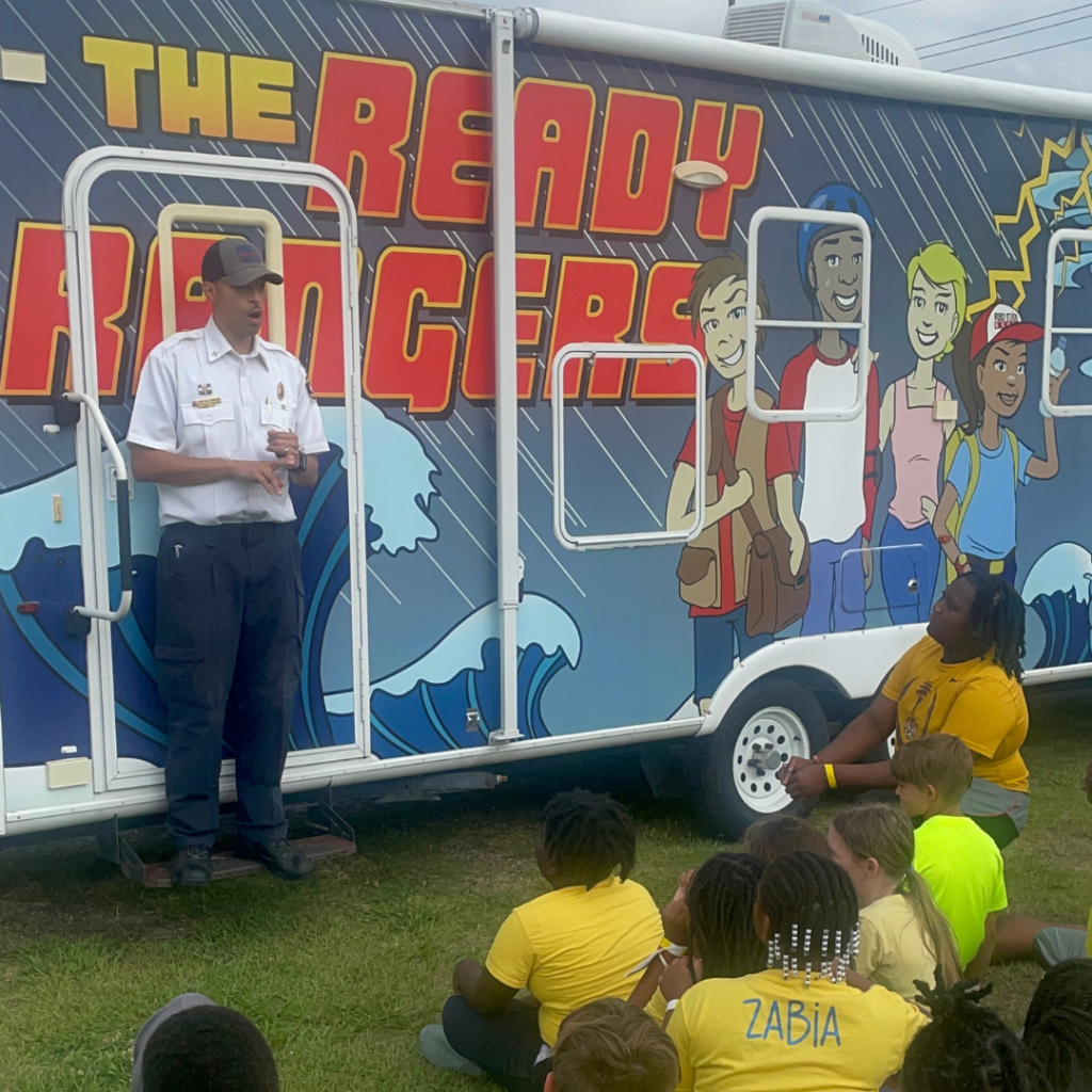 Baton Rouge Fire Department crew member stands in front of the Ready Rangers mobile as he speaks to field day participants.