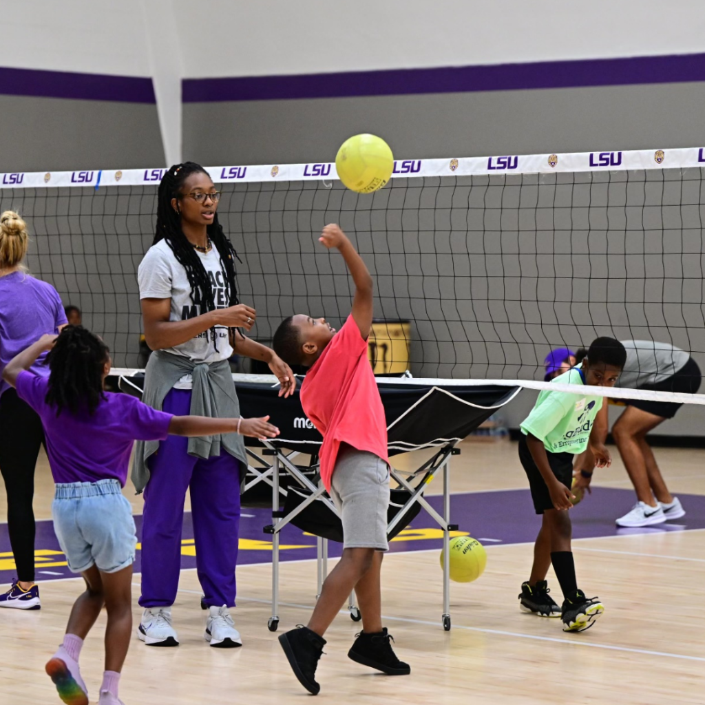 LSU volleyball player watches on as a Geaux Day participant volleys the ball over the net.
