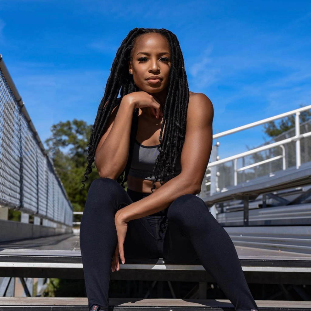 Photo of Natasha Hastings sitting while resting one elbow on her knee and smiling