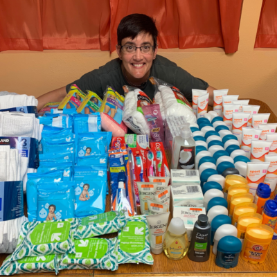 Photo of Alex Sachs smiling at a table full of nonperishable hygienic products