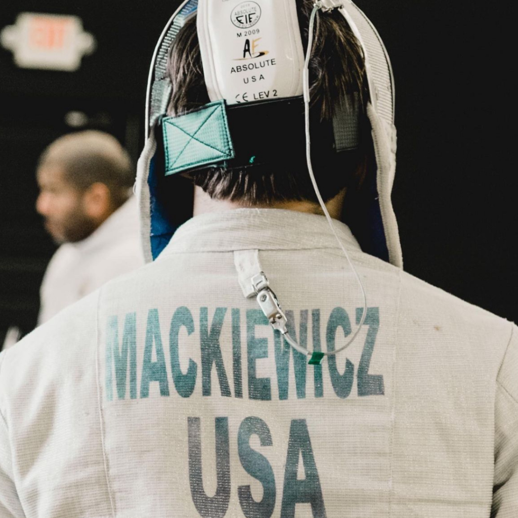 Photo of the back of Andrew Mackiewicz fencing uniform with the words "Mackiewicz" and "USA" visible in green,