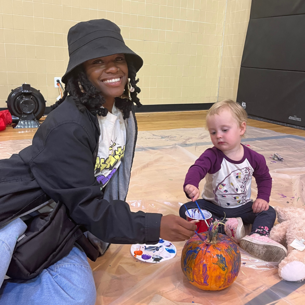 A Bowie State University student-athlete poses for a photo while painting a pumpkin with a toddler during Da Thanks B4 Giving event.