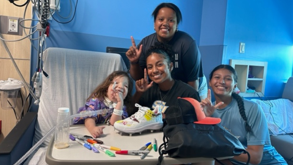 Southern University softball players pose with a new hospital friend as she customizes a spacial pair of cleats.
