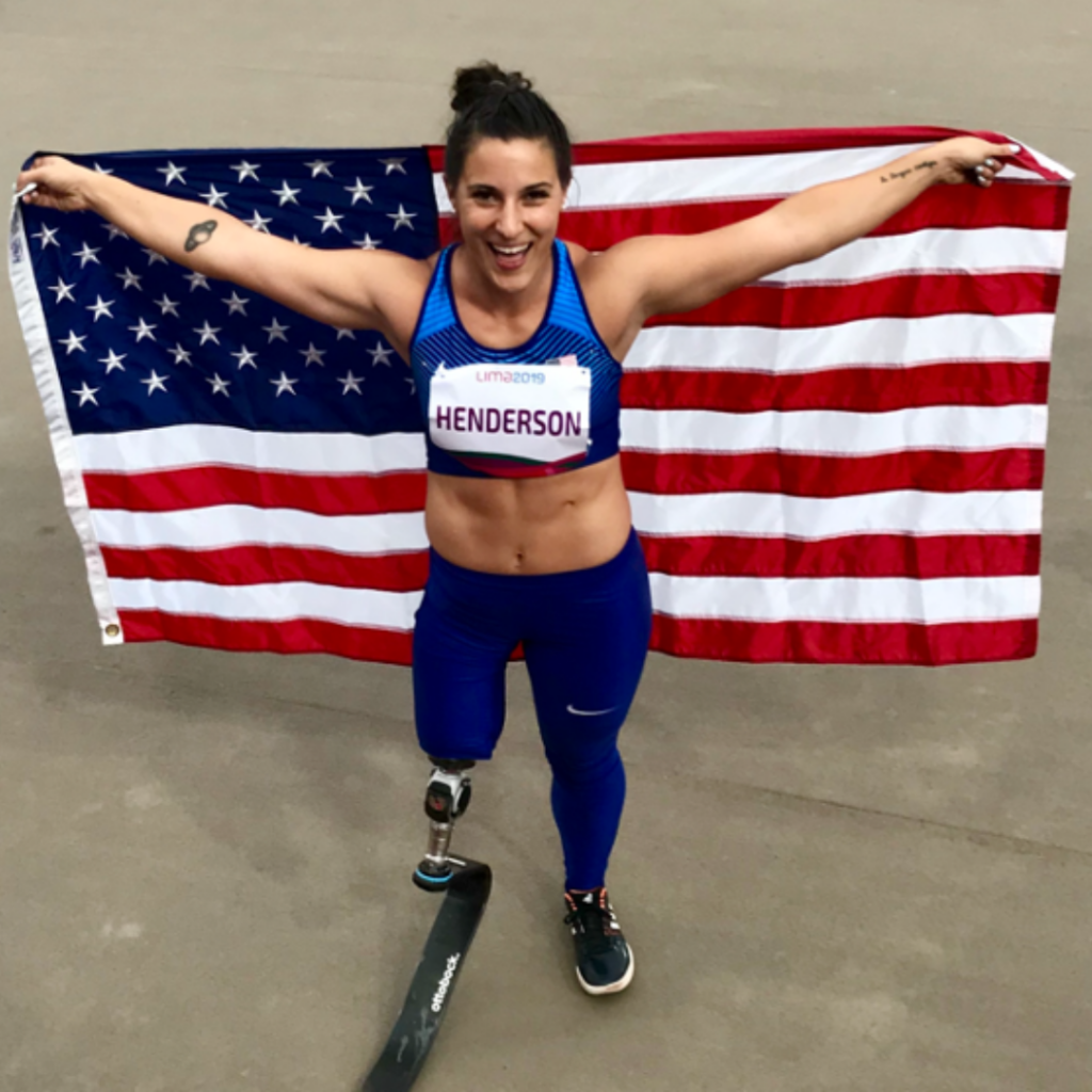 Photo of Paralympian Lacey Henderson smiling white holding the American flag behind her back.